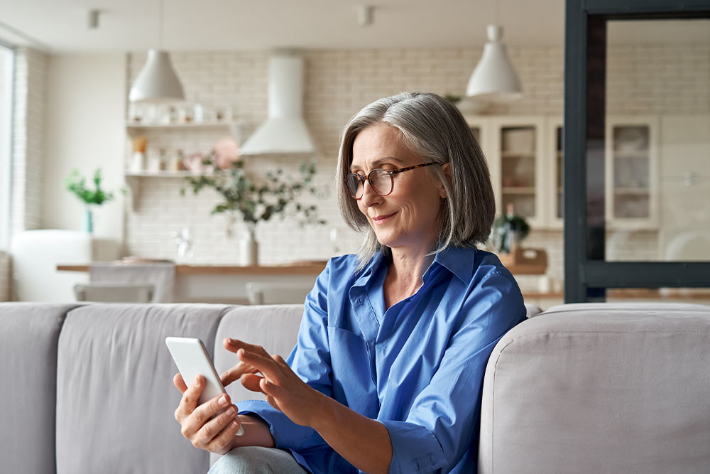 Frau sitzt auf der Couch und schaut auf ein Smartphone
